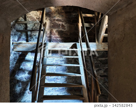 Ancient stone staircase inside dim underground tunnel with weathered wooden ladder and rustic beams, with ancient, staircase, stone, tunnel detail, showing underground, rustic, wooden, ladder context 142582843