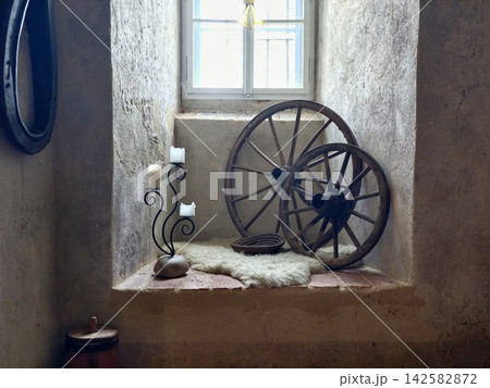 Rustic interior alcove with sunlit window, wagon wheel, candleholders, fur rug, aged stone walls, with rustic, interior, alcove, window detail, showing wagon, wheel, candleholder, candle context Rustic interior alcove with sunlit window, wagon wheel, candleholders, fur rug, aged stone walls, with rustic, interior, alcove, window detail, showing wagon, wheel, candleholder, candle context 142582872