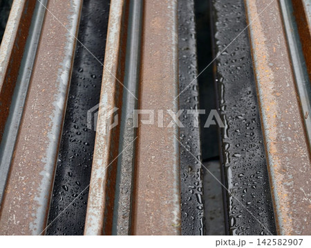 Close-up view of weathered rusted metal rails with water droplets on damp surfaces between aged iron bars, emphasizing texture and industrial detail, with rust, rusted, metal, rail detail Close-up view of weathered rusted metal rails with water droplets on damp surfaces between aged iron bars, emphasizing texture and industrial detail, with rust, rusted, metal, rail detail 142582907