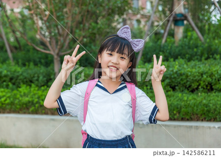 Cute Asian schoolgirl showing peace sign in sunlight, happy childhood and positive lifestyle concept 142586211