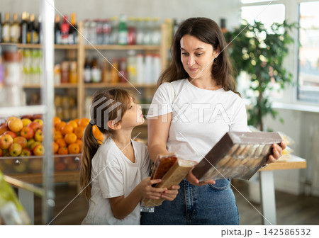 Mother consults with her daughter about which sweets to buy in the grocery section of supermarket - nougat or cookies 142586532