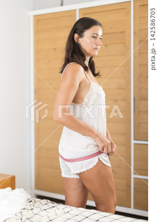 woman stands in the bedroom and thoughtfully measures her figure with a measuring tape woman stands in the bedroom and thoughtfully measures her figure with a measuring tape 142586705