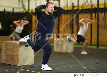 Bearded man performing Bulgarian split squats on box at gym 142587130