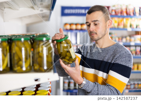 Adult man chooses pickled cucumbers in store 142587237