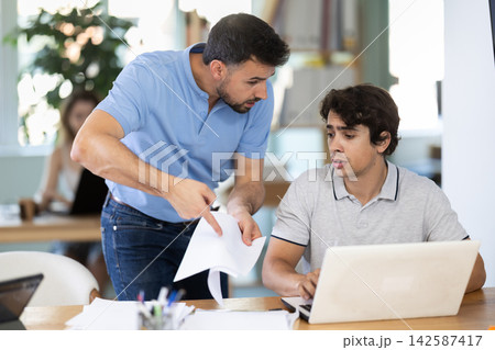 Man scolding sad male colleague working on laptop in office 142587417
