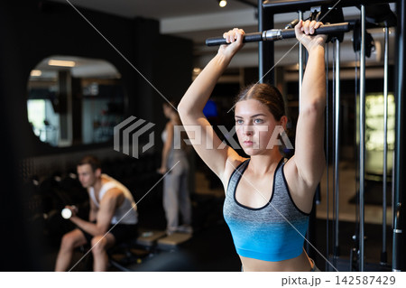 Sportive young girl training on cable exercise machine in gym Sportive young girl training on cable exercise machine in gym 142587429