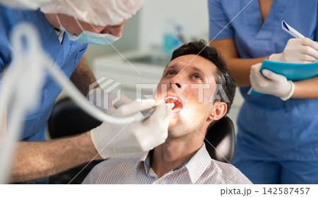During examination of male patients teeth, nurse listens to senior male doctors dentist instructions During examination of male patients teeth, nurse listens to senior male doctors dentist instructions 142587457
