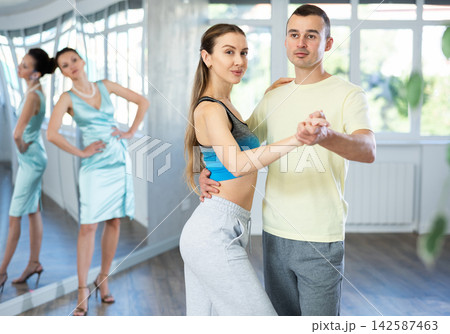 Couple in comfortable sports clothes waltz dancing during individual lesson Couple in comfortable sports clothes waltz dancing during individual lesson 142587463