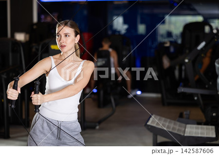 Active athlete young woman during exercises on crossover exercise machine with loops and weighting Active athlete young woman during exercises on crossover exercise machine with loops and weighting 142587606