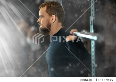 Young bearded man exercising with barbell during intense training 142587635