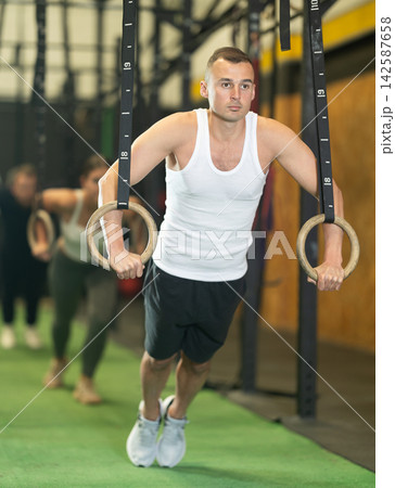 Man performing chest push-ups with gymnastic rings during workout in gym 142587658