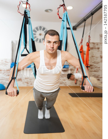 Man visitor performs exercises in hanging position on Pilates slings hammock Man visitor performs exercises in hanging position on Pilates slings hammock 142587705