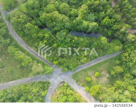 Aerial top down view of rural road intersection beside a freshwater pond and dense tropical forest. Green infrastructure, natural habitat and sustainable countryside landscape. Freshwater ecosystem. 142588534