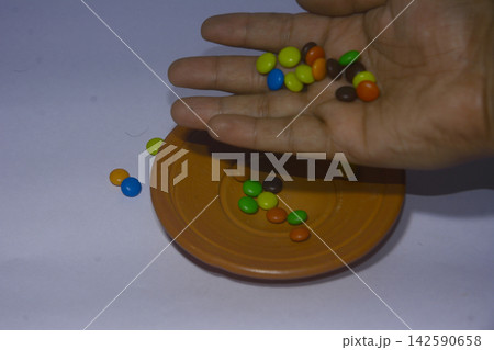 Person pouring colorful chocolate candies into a small clay bowl Person pouring colorful chocolate candies into a small clay bowl 142590658