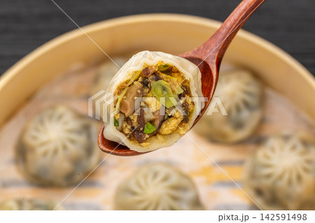 close-up of a steamed vegetarian bun on a wooden spoon, showing the rich vegetable and mushroom filling. 142591498
