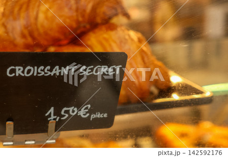 Croissant secret sign with pricing details in a display case. Fresh pastries are visible in the background, promoting french baking Croissant secret sign with pricing details in a display case. Fresh pastries are visible in the background, promoting french baking 142592176