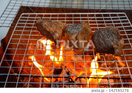 Grilled beef steak cooking on a charcoal fire. BBQ moments that bring people together. Grilled beef steak cooking on a charcoal fire. BBQ moments that bring people together. 142593278
