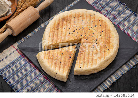 authentic Xinyang thick flatbread with a cut slice, crispy grilled Chinese wheat bread on a black platter. authentic Xinyang thick flatbread with a cut slice, crispy grilled Chinese wheat bread on a black platter. 142593514