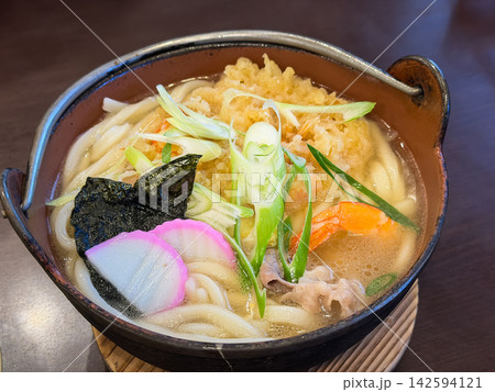 日本の冬によく食べられる鍋焼きうどん。かき揚げ風の海老天とネギと蒲鉾をトッピング。 142594121
