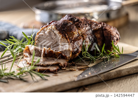 Tasty roasted pork neck with a crispy crust is garnished with fresh rosemary and sliced on a wooden board. This professional culinary shot will fit perfectly in cookbooks, restaurant menus, or food Tasty roasted pork neck with a crispy crust is garnished with fresh rosemary and sliced on a wooden board. This professional culinary shot will fit perfectly in cookbooks, restaurant menus, or food 142594447