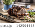 Tasty roasted pork neck with a crispy crust is garnished with fresh rosemary and sliced on a wooden board. This professional culinary shot will fit perfectly in cookbooks, restaurant menus, or food 142594448