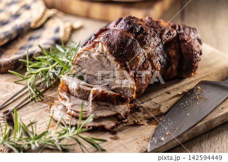 Tasty roasted pork neck with a crispy crust is garnished with fresh rosemary and sliced on a wooden board. This professional culinary shot will fit perfectly in cookbooks, restaurant menus, or food Tasty roasted pork neck with a crispy crust is garnished with fresh rosemary and sliced on a wooden board. This professional culinary shot will fit perfectly in cookbooks, restaurant menus, or food 142594449