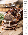 Detailed macro shot of juicy roasted pork shoulder with a perfectly browned crust. Tender meat slices lie on a wooden board next to fragrant rosemary, creating an inviting composition for any gourmet 142594451