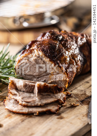 Detailed macro shot of juicy roasted pork shoulder with a perfectly browned crust. Tender meat slices lie on a wooden board next to fragrant rosemary, creating an inviting composition for any gourmet Detailed macro shot of juicy roasted pork shoulder with a perfectly browned crust. Tender meat slices lie on a wooden board next to fragrant rosemary, creating an inviting composition for any gourmet 142594451
