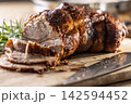 Tasty roasted pork neck with a crispy crust is garnished with fresh rosemary and sliced on a wooden board. This professional culinary shot will fit perfectly in cookbooks, restaurant menus, or food 142594452