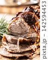Detailed macro shot of juicy roasted pork shoulder with a perfectly browned crust. Tender meat slices lie on a wooden board next to fragrant rosemary, creating an inviting composition for any gourmet 142594453