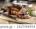 Tasty roasted pork neck with a crispy crust is garnished with fresh rosemary and sliced on a wooden board. This professional culinary shot will fit perfectly in cookbooks, restaurant menus, or food 142594454