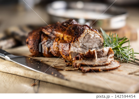 Tasty roasted pork neck with a crispy crust is garnished with fresh rosemary and sliced on a wooden board. This professional culinary shot will fit perfectly in cookbooks, restaurant menus, or food Tasty roasted pork neck with a crispy crust is garnished with fresh rosemary and sliced on a wooden board. This professional culinary shot will fit perfectly in cookbooks, restaurant menus, or food 142594454