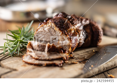 Tasty roasted pork neck with a crispy crust is garnished with fresh rosemary and sliced on a wooden board. This professional culinary shot will fit perfectly in cookbooks, restaurant menus, or food 142594455