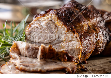Tasty roasted pork neck with a crispy crust is garnished with fresh rosemary and sliced on a wooden board. This professional culinary shot will fit perfectly in cookbooks, restaurant menus, or food Tasty roasted pork neck with a crispy crust is garnished with fresh rosemary and sliced on a wooden board. This professional culinary shot will fit perfectly in cookbooks, restaurant menus, or food 142594456