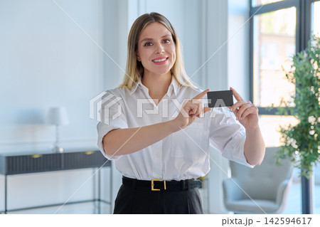 Portrait of smiling business woman holding blank credit card standing in modern light office Portrait of smiling business woman holding blank credit card standing in modern light office 142594617