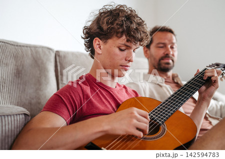 Father teaching teenage son to play guitar at home. 142594783