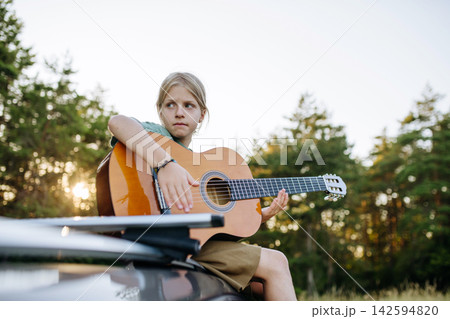 Child learning to play guitar outdoors during summer camping. Child learning to play guitar outdoors during summer camping. 142594820