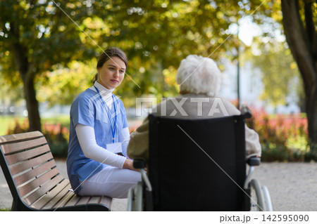 Disabled elderly woman in wheelchair holding hands with her nurse, talking about her problems. Disabled elderly woman in wheelchair holding hands with her nurse, talking about her problems. 142595090
