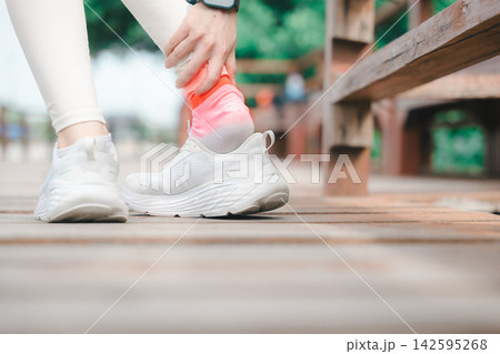 Sportswoman with Achilles tendon pain ache, trauma from running, holds foot during training, representing health medicine body problem, runner in white sneakers on wooden walkway 142595268