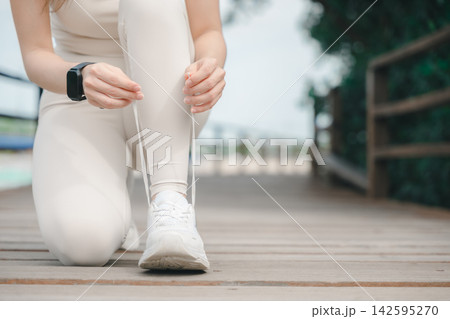 Fit sport runner woman tying shoelace, healthy lifestyle people training exercise, female athlete in white sneakers preparing for outdoor workout on wooden bridge Fit sport runner woman tying shoelace, healthy lifestyle people training exercise, female athlete in white sneakers preparing for outdoor workout on wooden bridge 142595270