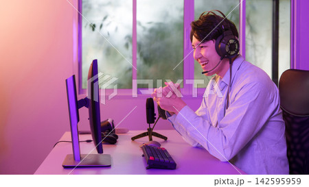 Asian man wearing headset smiling at computer monitor for video gaming and live streaming 142595959