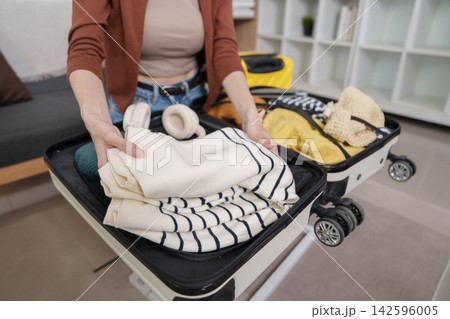 Cropped shot of woman packing sweater into suitcase for travel preparation Cropped shot of woman packing sweater into suitcase for travel preparation 142596005