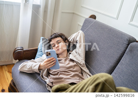 Lazy young zoomer woman scrolling smartphone lying on sofa, distracted by digital addiction at home 142599816