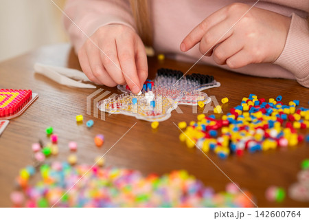 Child creating colorful bead art at a wooden table during a fun creative craft activity 142600764