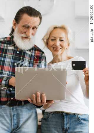 A smiling senior couple uses a laptop and credit card for convenient online shopping from home A smiling senior couple uses a laptop and credit card for convenient online shopping from home 142601100