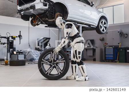 A humanoid robot is shown in a garage, holding a car tire near a vehicle suspended on a lift, suggesting automated automotive repair A humanoid robot is shown in a garage, holding a car tire near a vehicle suspended on a lift, suggesting automated automotive repair 142601149
