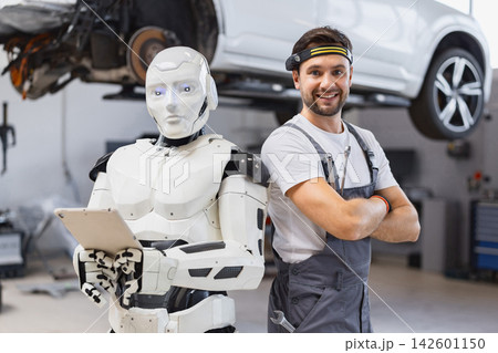 A smiling mechanic stands beside a humanoid robot holding a tablet in a modern automotive repair facility A smiling mechanic stands beside a humanoid robot holding a tablet in a modern automotive repair facility 142601150