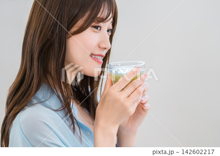 栄養たっぷりのグリーンスムージーを楽しむ若い女性。健康と美容を意識した朝の習慣 栄養たっぷりのグリーンスムージーを楽しむ若い女性。健康と美容を意識した朝の習慣 142602217