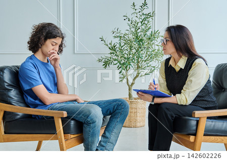 Sad teenage boy talking to female psychologist during therapy session. 142602226