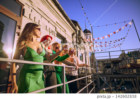 Female friends share beer and conversation on balcony decorated with bunting Female friends share beer and conversation on balcony decorated with bunting 142602838